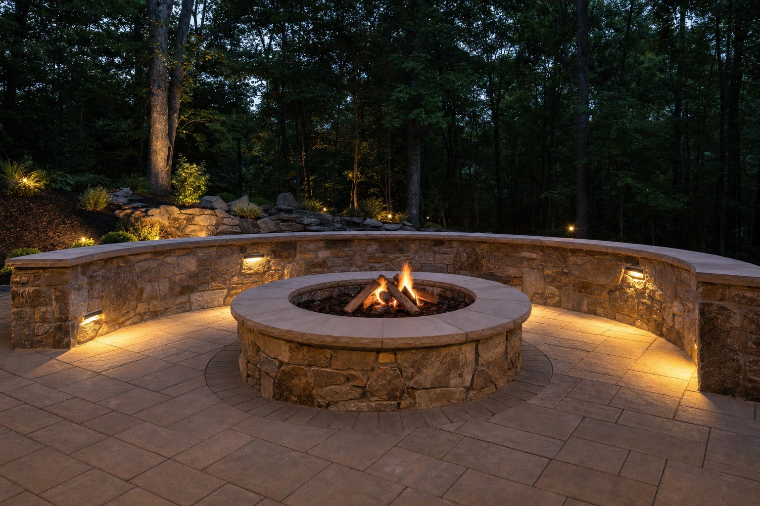 Natural stone fire pit and seating wall on a paver patio at dusk